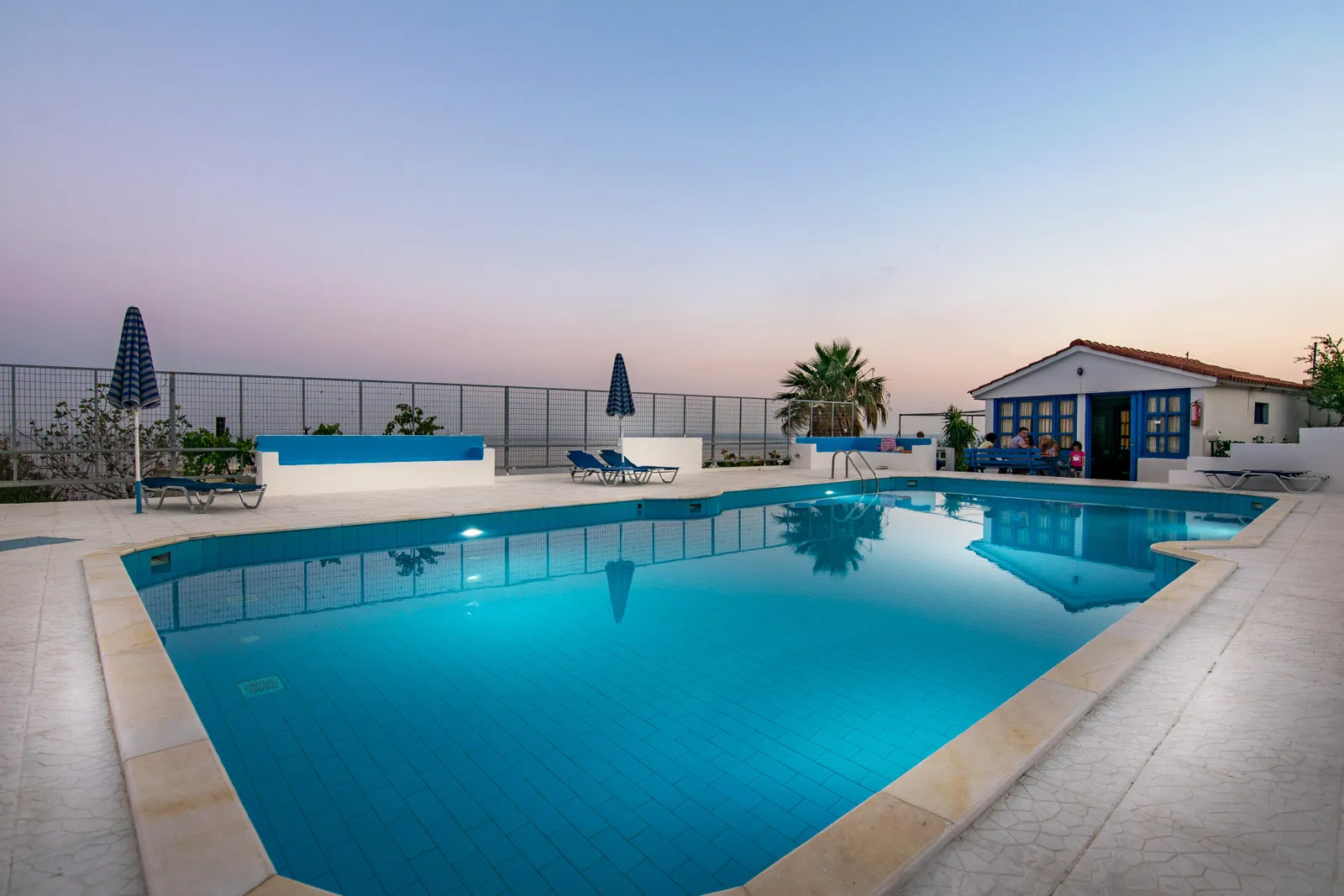 The Creta Sky pool glowing turquoise beneath a pink and lavender dusk sky